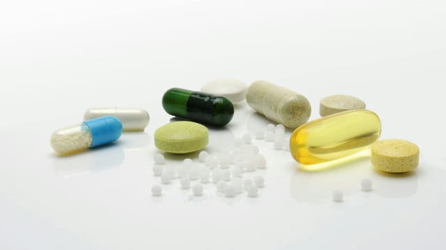 Close-up of various pills and capsules on a white surface, representing healthcare.