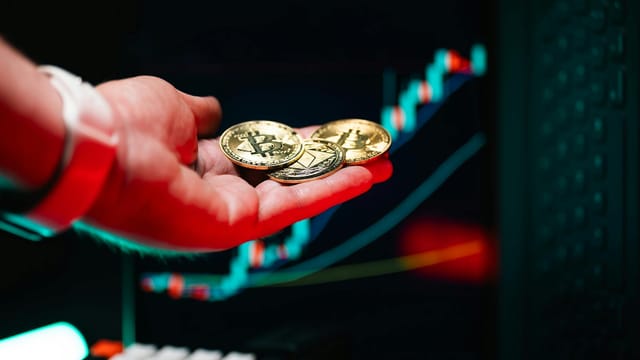 Close-up of hand holding cryptocurrency coins with trading chart in background.