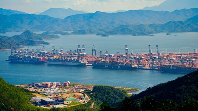 Aerial shot of a bustling shipping port amidst mountains by the water, showcasing international trade.