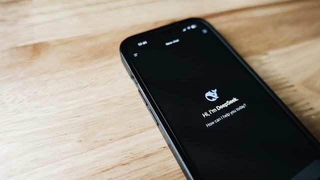Close-up of a smartphone with DeepSeek virtual assistant on screen, placed on a wooden surface.
