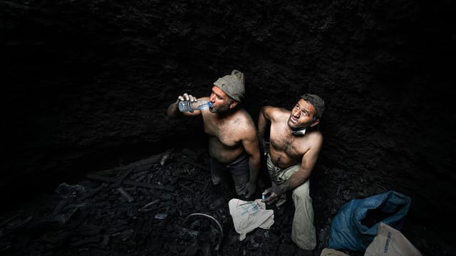 Two shirtless miners taking a break in a dark coal mine in Iran.
