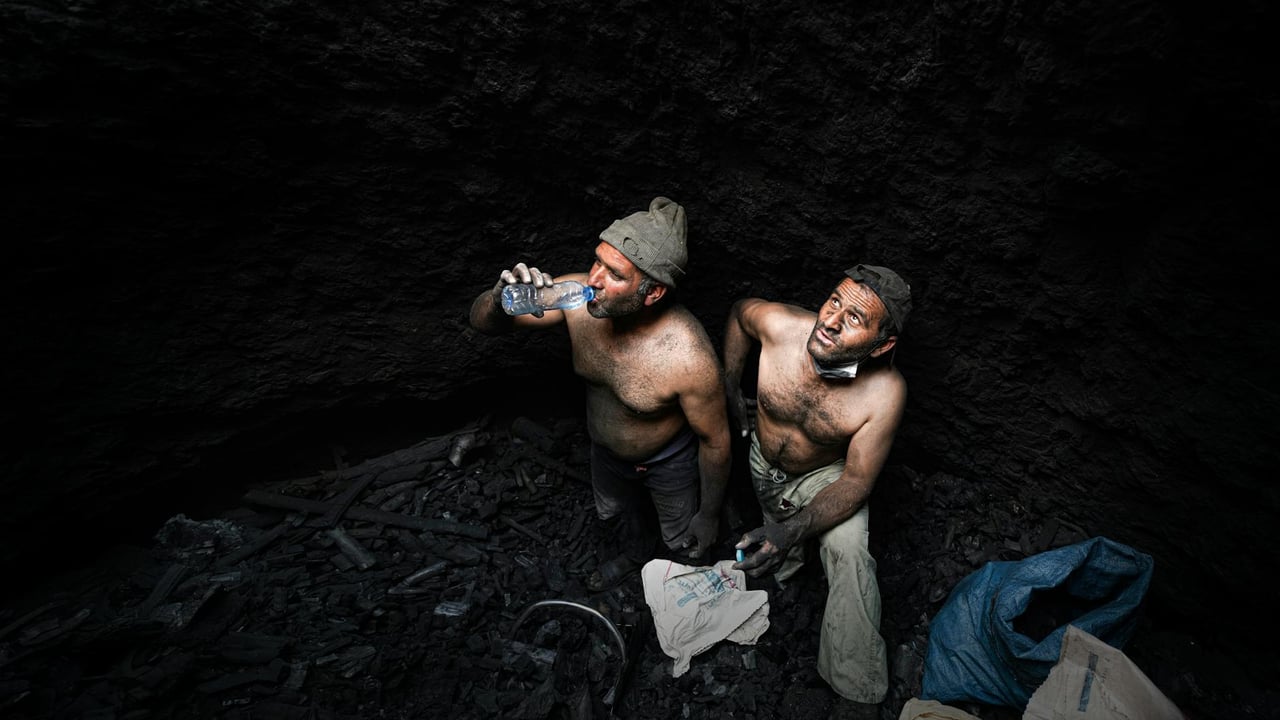 Two shirtless miners taking a break in a dark coal mine in Iran.