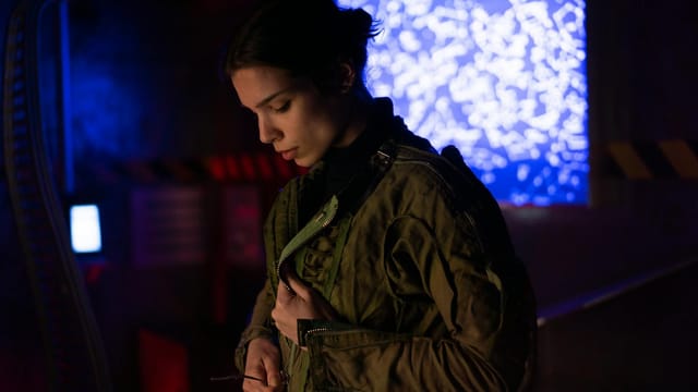 A woman in a sci-fi environment wearing a futuristic jacket, surrounded by technology and lights.