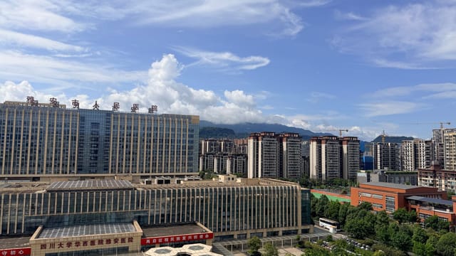 A panoramic view of a contemporary hospital and urban buildings in Sichuan under a bright blue sky.