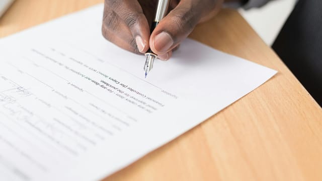 A hand holding a pen signing a document close-up on a desk, symbolizing agreement or contract finalization.