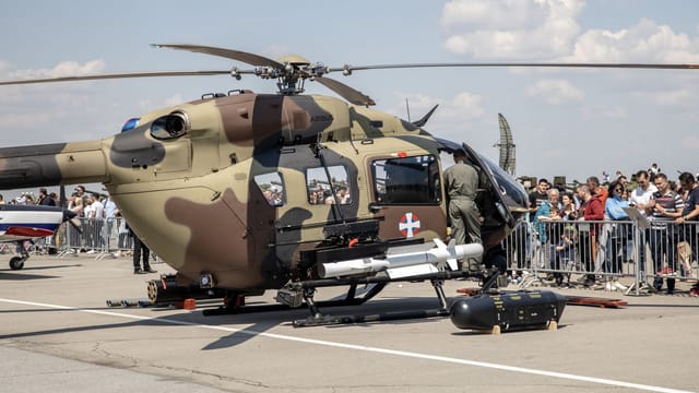 Army helicopter showcased at airshow with crowd in attendance on a sunny day.