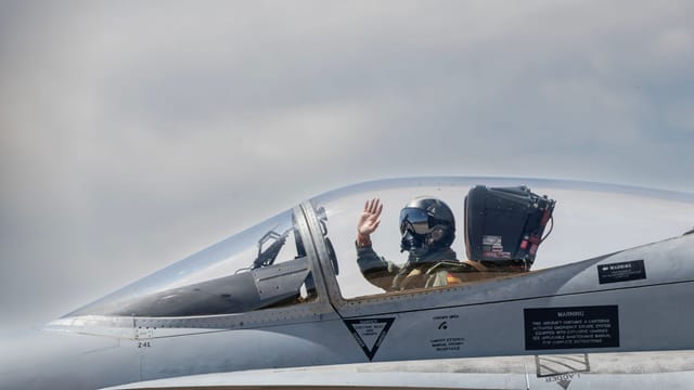 A military pilot salutes from a fighter jet cockpit, ready for takeoff.