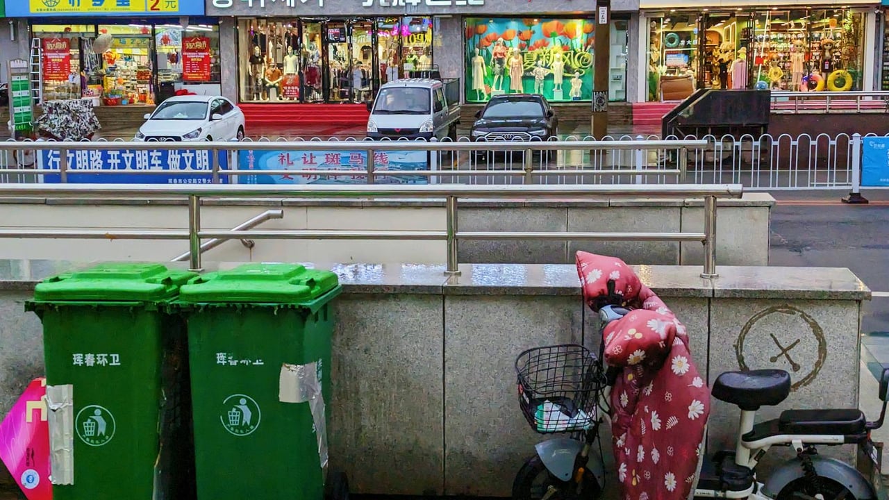 Street view in Yanbian, Jilin, featuring a bicycle and recycling bins against a shopping complex backdrop.