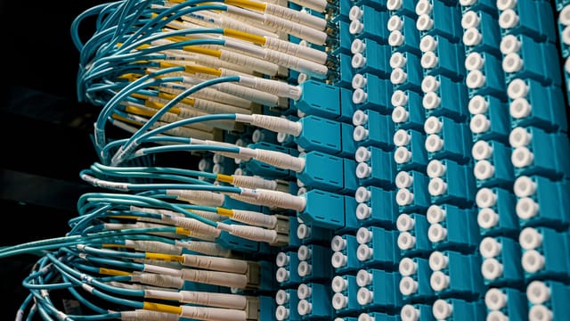 Detailed view of fiber optic patch cables connecting to a blue patch panel in a data center.