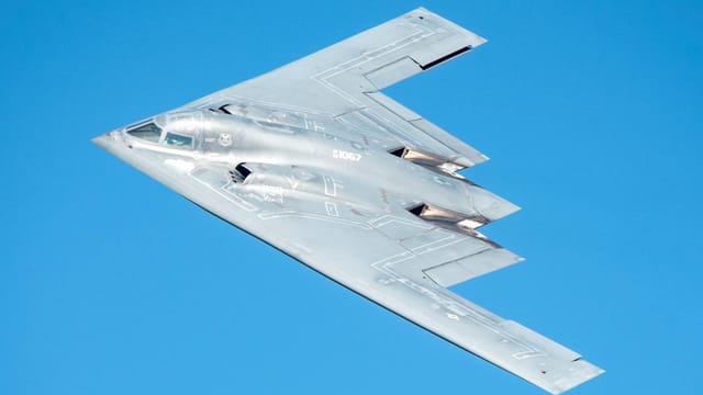 A high-resolution image of a B-2 stealth bomber flying against a clear blue sky.