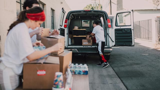 Volunteers organize and load boxes of donated supplies into a van for distribution.
