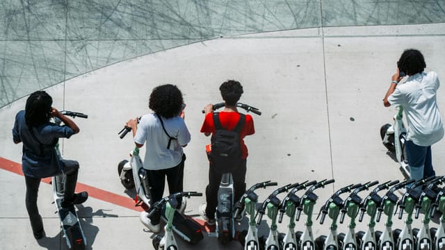 Group of young adults using electric scooters on a sunlit urban pavement.