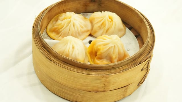 Close-up of steamed dumplings in a bamboo basket on white background, perfect for Asian cuisine themes.