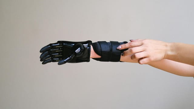 Close-up of a person adjusting a high-tech prosthetic arm against a gray background.
