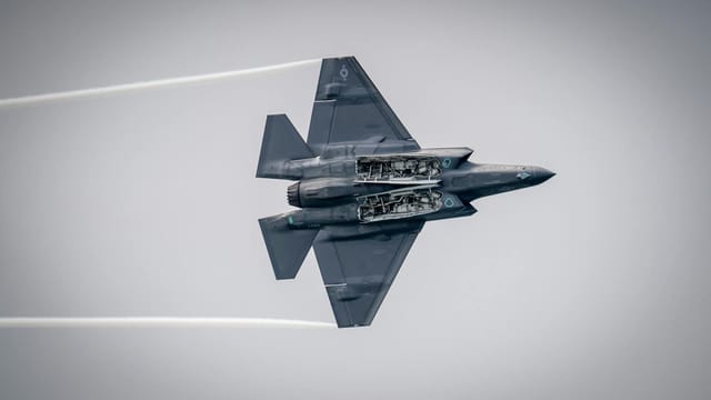 An F-35 fighter jet soaring above Huntington Beach, showcasing its underside in flight.