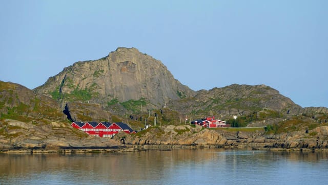 Picturesque red houses along a rocky coastline with clear blue skies and tranquil water.