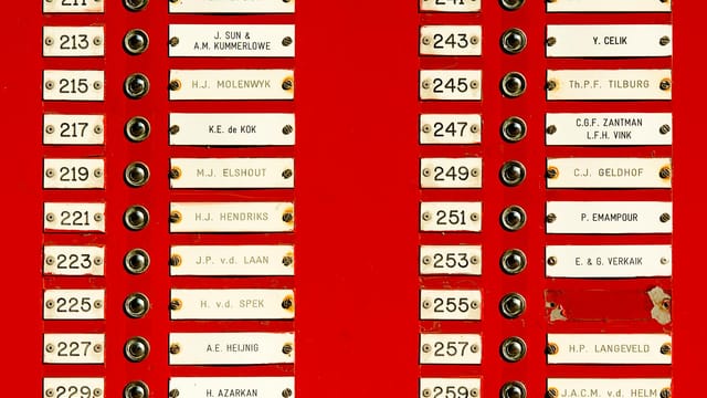 Close-up of a red doorbell panel with multiple nameplates and buttons in a building.