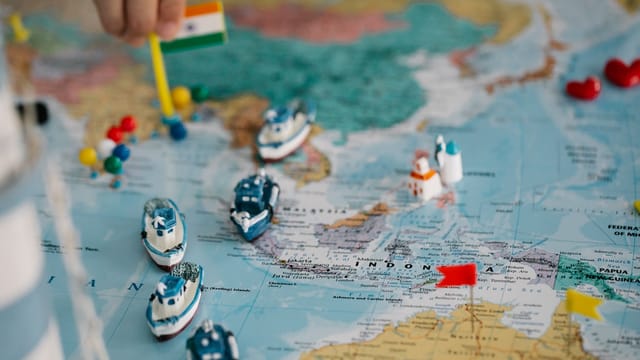 A detailed view of a world map with tiny model ships and flags indicating locations, highlighting global trade routes.