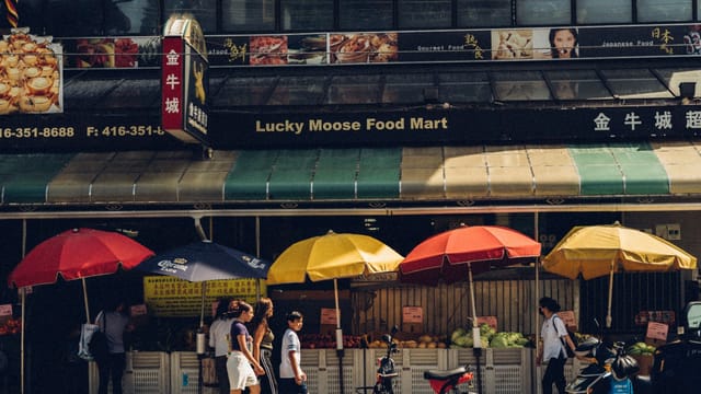 Vibrant market street scene in daylight featuring colorful umbrellas and pedestrians.