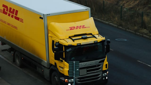 Yellow DHL delivery truck driving along a city road showcasing logistics in action.