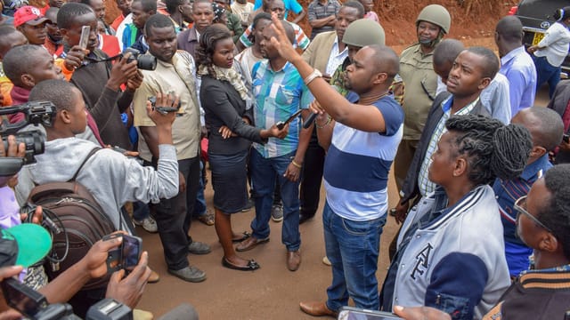 A diverse group discusses community issues with a politician in an outdoor setting.