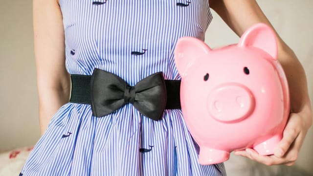 Close-up of a woman in a striped dress holding a pink piggy bank, symbolizing savings and financial planning.