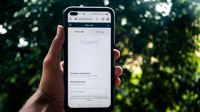 A person uses ChatGPT on a smartphone outdoors, showcasing technology in daily life.