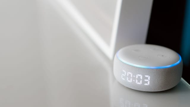 Close-up of a smart speaker with a digital clock display on a minimalist surface.