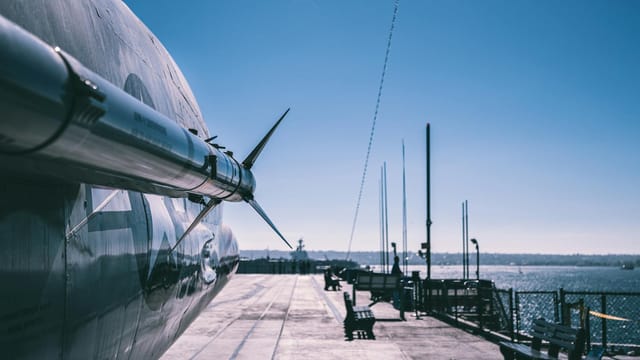 Aerial view of missile-equipped military aircraft on naval ship deck in San Diego harbor.