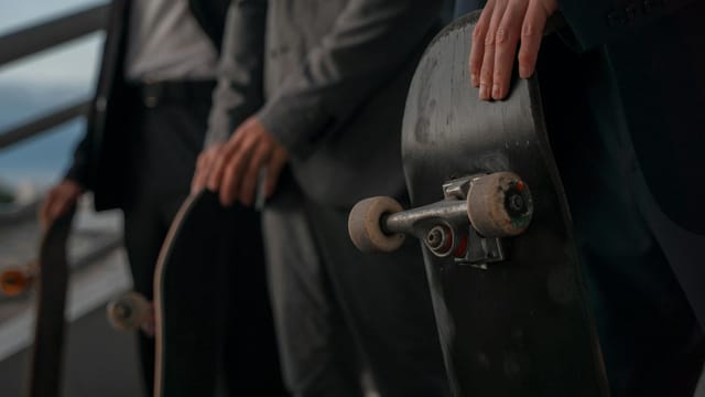 Close-up of business professionals in suits holding skateboards, blending corporate and urban cultures.