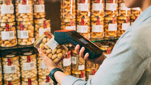 Individual scanning QR codes on jars in a store with a handheld device.