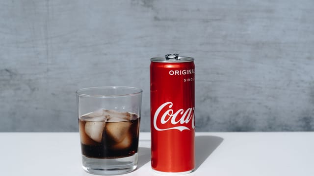 Chilled Coca-Cola can and drink with ice cubes in glass on minimalistic surface.