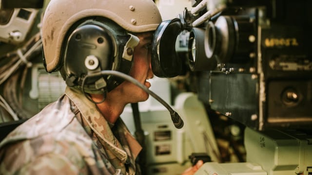 A soldier in uniform operates military equipment inside a vehicle, showcasing modern military technology.