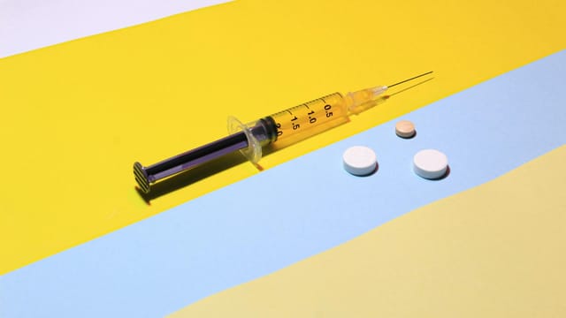 A syringe and pills on a vibrant yellow and blue background, depicting healthcare theme.