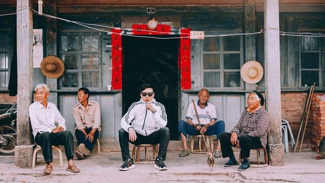 A diverse group of people sitting outside a rustic building with traditional decorations, conveying community life.