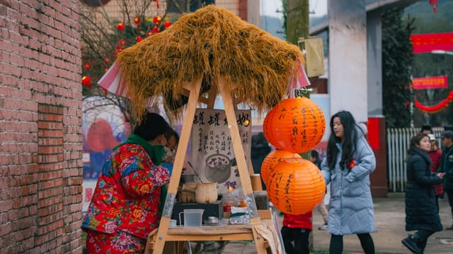 Asian festival scene featuring a vibrant street food stall with lanterns and people around.