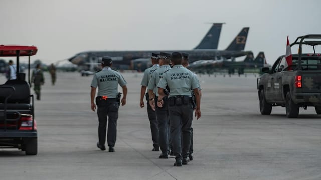 National Guard officers patrolling an airport tarmac with planes in the background.
