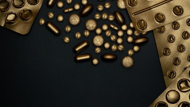 Close-up of gold blister packs and pills arranged on a black surface.