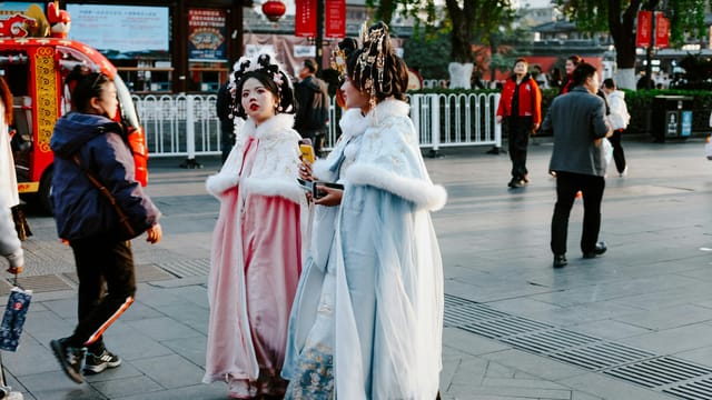 People in traditional attire stroll through a vibrant Nanjing street in autumn.
