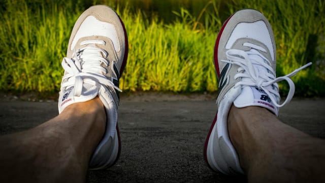A person enjoys a quiet moment outdoors wearing sneakers against a green backdrop.