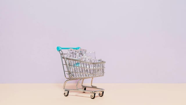 A small shopping cart filled with ice cubes against a pastel backdrop, perfect for retail or concept themes.