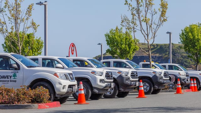 Fleet of utility trucks parked in an outdoor lot with safety cones and trees.