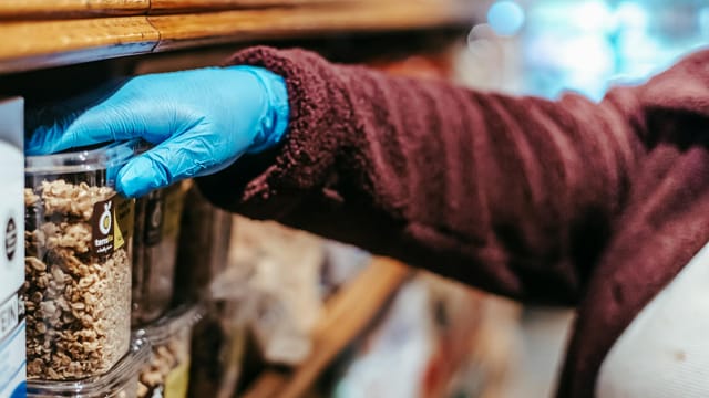 Crop anonymous woman in latex gloves picking food in plastic container while shopping in grocery store