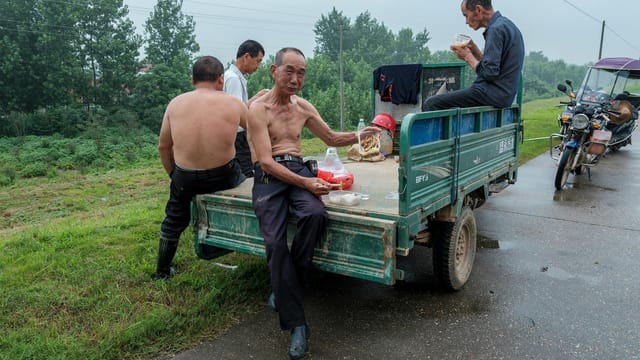 Men relaxing during a work break on a truck in a rural setting.