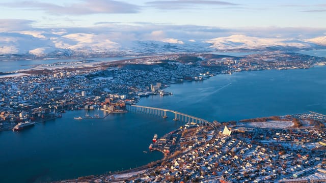 Panoramic aerial view of Tromsø, Norway, showcasing snow-capped mountains and the iconic Arctic Cathedral.