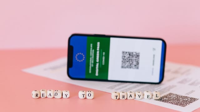 Smartphone displaying digital green pass on a pink surface with travel beads.