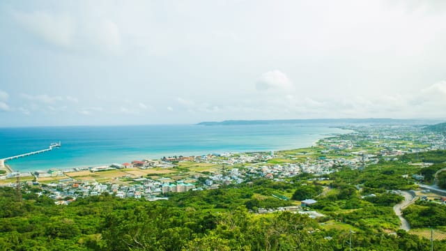 Calm turquoise water of ocean washing shore with small town and green tropical forest under cloudy sky