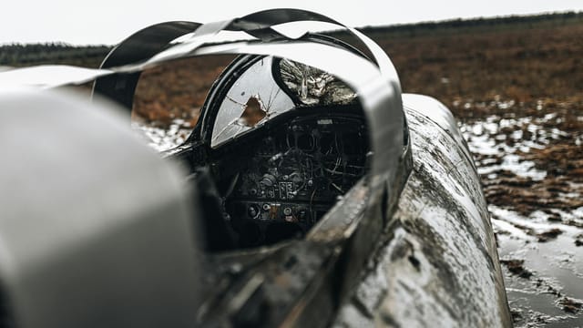 A damaged cockpit of a military aircraft crash site in a desolate field.