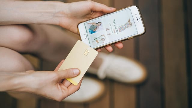 Hands holding smartphone and credit card for online shopping on a wooden floor.