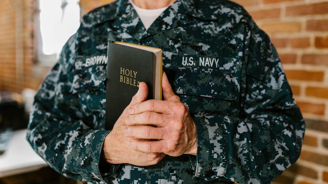 A U.S. Navy sailor in uniform holding a Holy Bible, symbolizing faith and service.